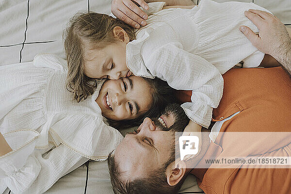 Happy father embracing cute daughters on bed at home