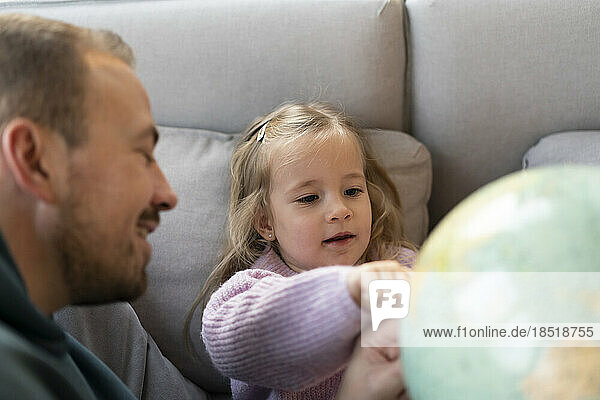 Tochter schaut mit Vater auf dem Sofa zu Hause auf den Globus