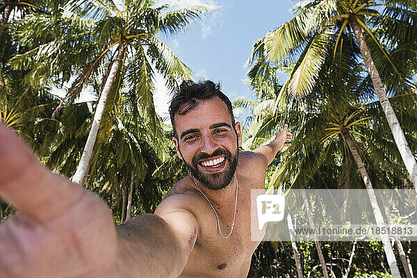 Glücklicher Mann  der ein Selfie mit tropischen Bäumen im Hintergrund macht