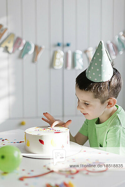 Boy touching birthday cake on table at home