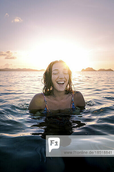 Happy woman with eyes closed swimming in sea at sunset