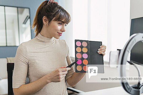 Influencer showing make-up palette on tutorial at home