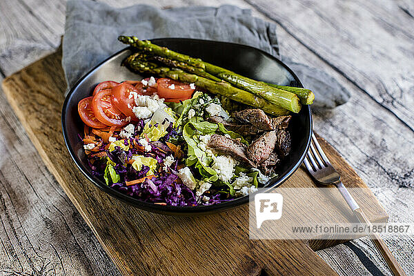 Bowl of salad with steak  asparagus  tomatoes  shredded red cabbage  lettuce and feta cheese
