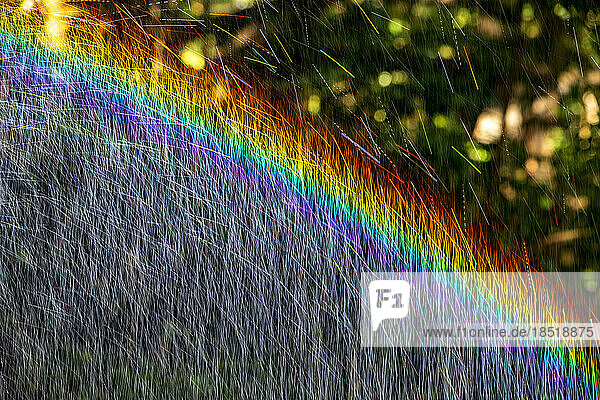 Langzeitbelichtung eines Wasserstrahls  der mit regenbogenfarbenem Licht bedeckt ist
