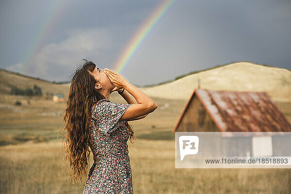 Optical illusion of rainbow coming out from mouth of woman standing in field