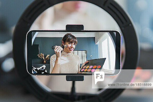Smart phone screen mounted on ring light with vlogger filming make-up vlog