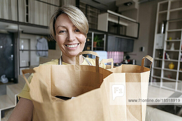 Happy mature woman holding paper bags at home
