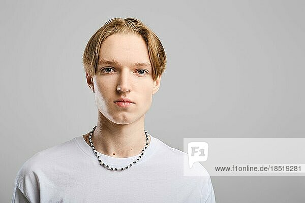 Closeup Porträt von ernsten jungen Mann in weißem TShirt über grauem Hintergrund Studio