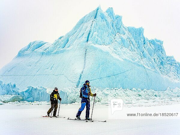Ski tourers in front of iceberg in frozen Kong Oscar Fjord  Tasiilaq  Ammassalik Island  Kommuneqarfik Sermersooq  East Greenland  Greenland  North America
