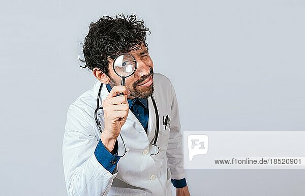 Doctor with magnifying glass looking at the camera. Doctor holding magnifying glass and looking at camera on isolated background