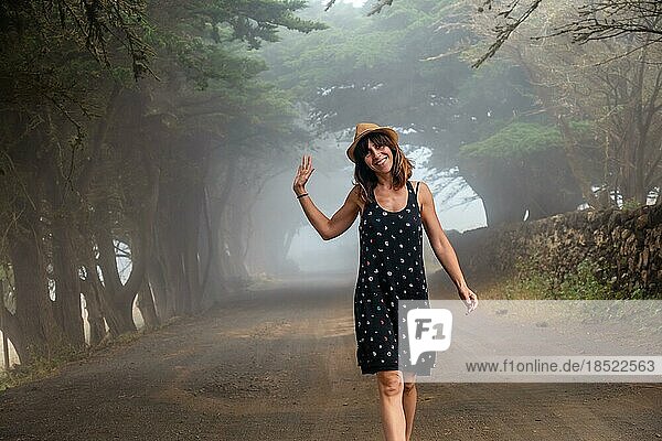 Eine Frau genießt den Spaziergang durch die nebligen Bäume in Richtung des Wacholderwaldes auf El Hierro. Kanarische Inseln