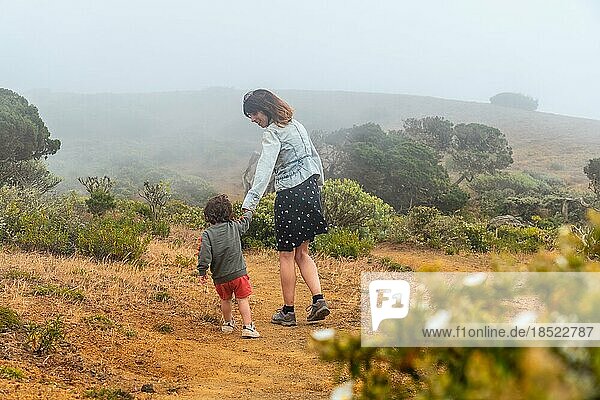 Mutter und Sohn spazieren mit Blumen zu einem vom Wind verdrehten Sabinar Baum auf El Hierro. Kanarische Inseln