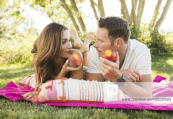 Couple eating peaches during picnic in park 