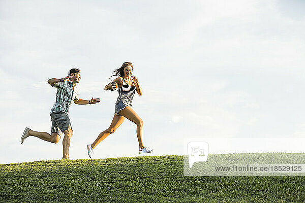 Woman and man running on grassy hill in park 
