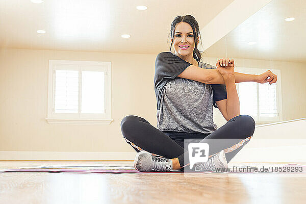 Smiling woman sitting on floor and stretching arm