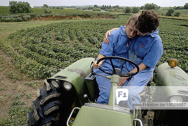 Woman and her daughter rest on a farm tractor while doing chores; Bennett  Nebraska  United States of America