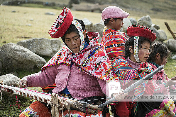 Frau sitzt bei der Arbeit an einer traditionellen Handweberei  mit Kindern an ihrer Seite; Cusco  Peru