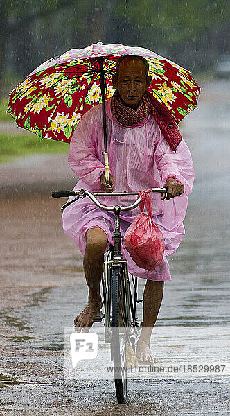 Kambodschanischer Mann mit Regenschirm auf einem Fahrrad im Regen; Siem Reap  Kambodscha