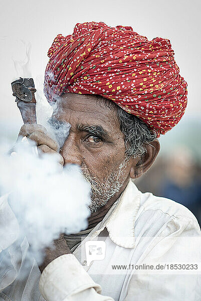 Nahaufnahme eines indischen Mannes  der eine Chillum-Pfeife raucht und den Rauch aus dem Mund bläst; Pushkar  Rajasthan  Indien