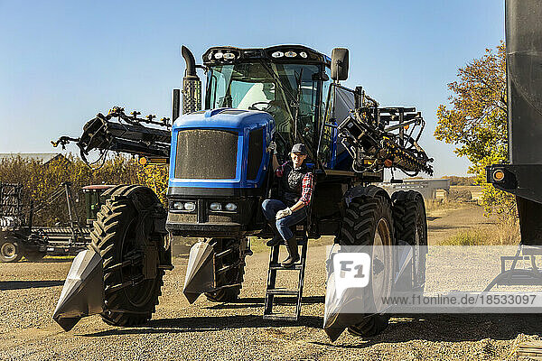 Porträt einer Landwirtin  die auf den Stufen eines Traktors mit Sämaschinenanbau sitzt; Alcomdale  Alberta  Kanada