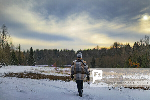 Junger Mann geht über ein verschneites Feld auf dem Lande; Surrey  British Columbia  Kanada