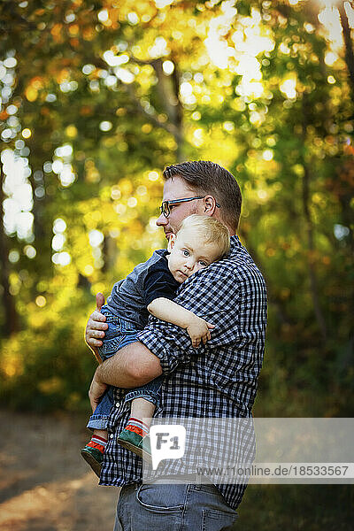 Father holds and comforts his baby boy outdoors in a park in autumn; Edmonton  Alberta  Canada