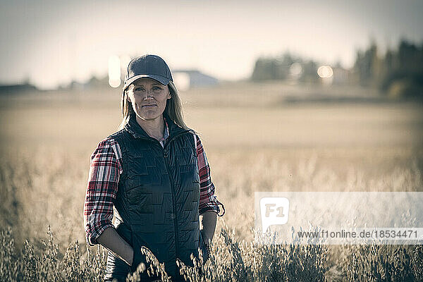 Nahaufnahme einer reifen Bäuerin in einem Getreidefeld  die während der Ernte bei Sonnenuntergang für die Kamera posiert; Alcomdale  Alberta  Kanada