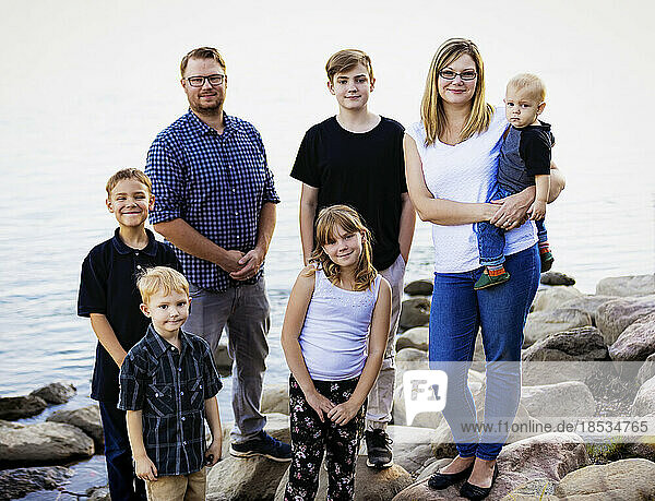 Outdoor portrait of a family with five young children standing on rocks beside a tranquil lake; Edmonton  Alberta  Canada