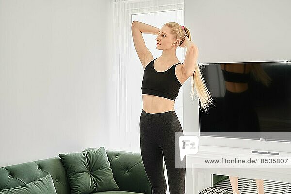Active blonde woman does twisting exercises in bright apartment
