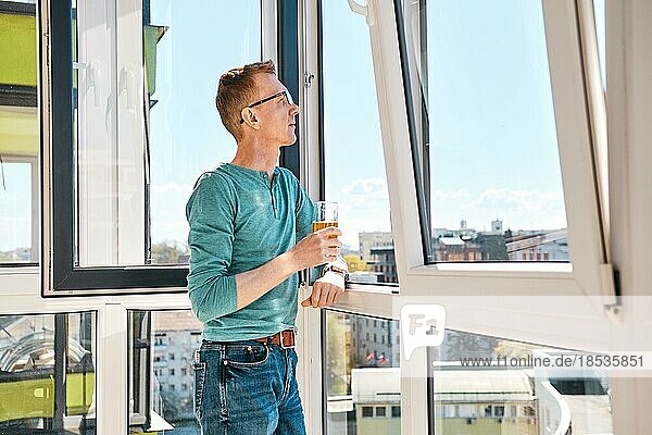 Mann mittleren Alters mit Brille steht auf dem Balkon eines Hochhauses