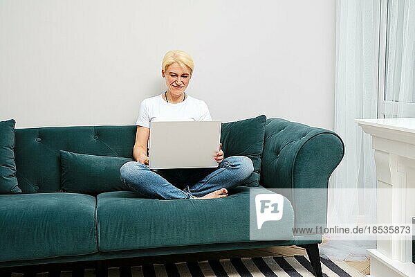 Eine reife Frau entspannt sich auf dem Sofa  während sie Filme anschaut und auf ihrem Laptop im Internet surft  und genießt den Komfort eines unabhängigen häuslichen Lebens