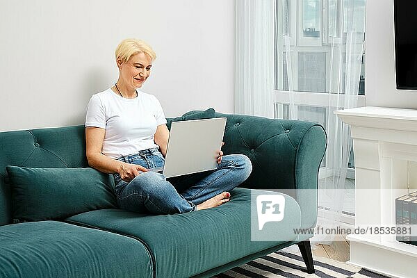 Eine Frau mittleren Alters chattet online mit einer Freundin in ihrer neuen Wohnung. Konzept des cleveren Alterns und der Anpassung an die neue Realität