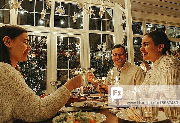 Ein glückliches Familienpaar stößt mit Sektgläsern an  während es Silvester oder Weihnachten mit Freunden feiert und an einem festlich gedeckten Tisch mit traditionellen Speisen und brennenden Kerzen sitzt