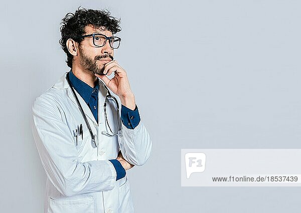 Young doctor thinking and looking up isolated. Pensive doctor man looking up isolated  Doctor thinking with hand on chin