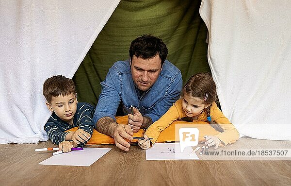 Glücklicher Vater mit kleiner Tochter und Sohn Zeichnung drinnen in handgemachten Wigwam. Familie  Spaß und Hobby Konzept