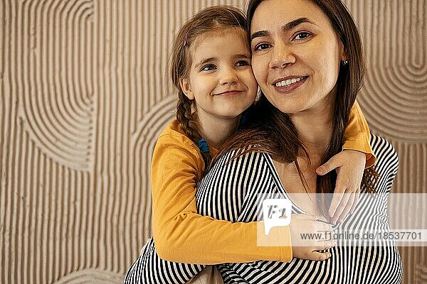 Mama und kleine Tochter umarmen auf beige Hintergrund mit Kopie Raum  glückliche Familie  Elternschaft. Konzept der mütterlichen Liebe und Fürsorge