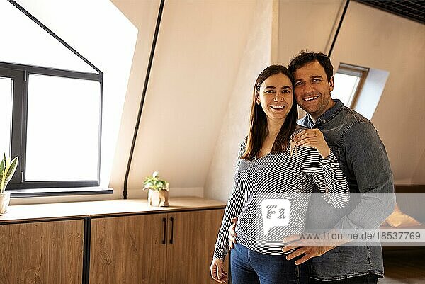 Hauseigentum. Porträt des glücklichen jungen Paares  das den Schlüssel in der neuen Wohnung hält  ein fröhlicher Mann und eine fröhliche Frau  die sich nach dem Umzug in die Wohnung umarmen. Versicherung  Immobilien  Hypothek Konzept