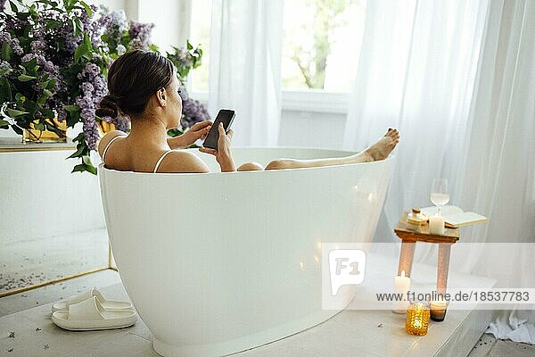 Seitenansicht Porträt einer hübschen asiatischen Frau Tippen Nachricht auf Handy  während ein Bad zu Hause