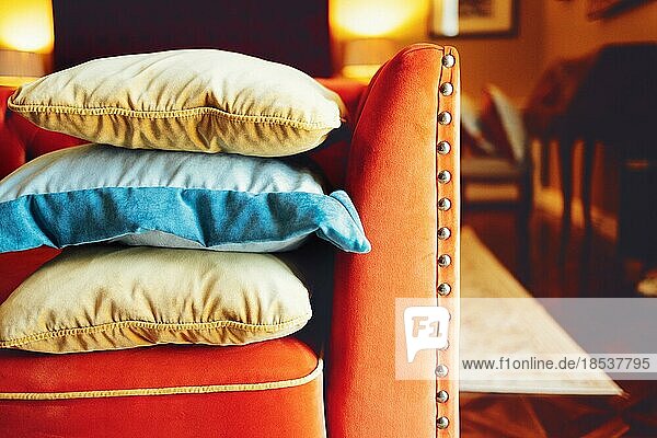 Orange  blaue und beige Kissen auf einem roten bequemen Sofa in einer schicken Wohnzimmereinrichtung. Nahaufnahme