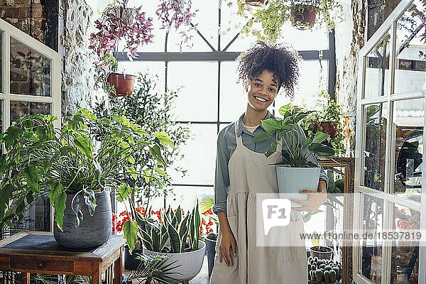 Glückliche Pflanze Dame. Junge afroamerikanische Frau Pflanzenliebhaberin  die sich um eine Zimmerpflanze kümmert. Mädchen bewässert eine Topfpflanze mit glücklichem Lächeln