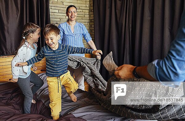 Happy family multiethnic mother  father and kids  son and daughter  laughing  playing  fights pillows and jumping in bed in bedroom at home in the morning