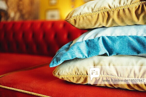 Orange  blaue und beige Kissen auf einem roten bequemen Sofa in einer schicken Wohnzimmereinrichtung. Nahaufnahme