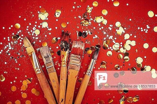 Set von bunten Künstlerpinseln. Leuchtend roten Hintergrund mit silbernen Glitzer und Gold runden Konfetti. Gemalte Pinsel. Kopierraum. Feiern und Kunstkonzept