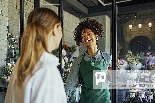 Happy black woman entrepreneur standing in plant store selling fresh flowers to client. Young blond girl buy a fresh bouquet from florist. Smiling african woman botanist  selling flowers