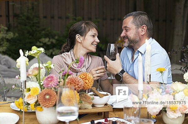 Happy couple talking and flirting in the terrace garden holding glasses with wine. People toasting together at outdoors wedding summer party