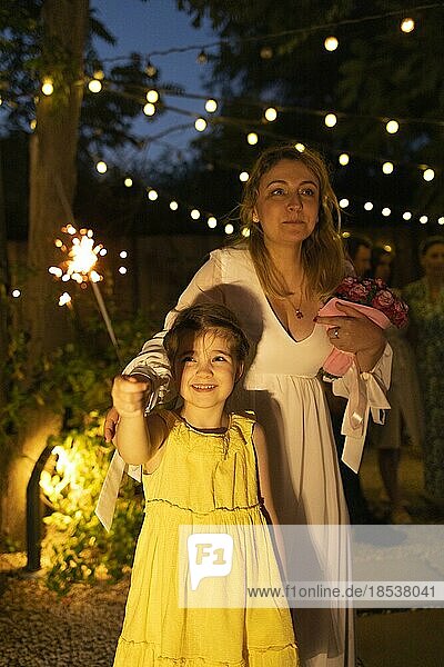 Mutter Braut mit kleinen süßen Tochter hält brennende Bengalische Lichter im Freien auf der Hochzeitsparty. Liebe und Feier Konzept