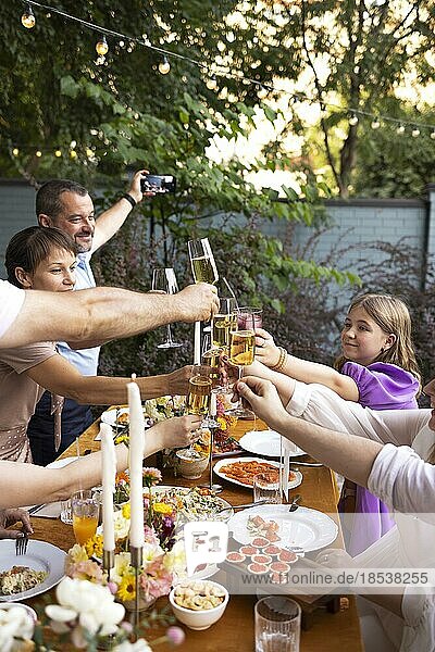 HAppy friends saying cheers and showing their champagne glasses full of sparkling wine to each other whilst enjoying an outdoor wedding party on a backyard restaurant at sunset
