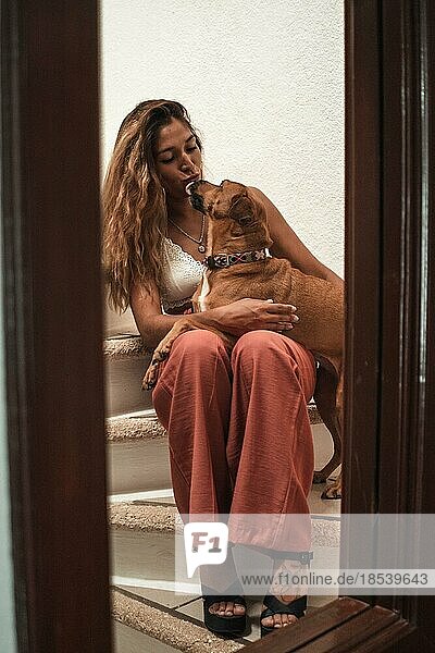 Beautiful young latina hugging her dog showing her affection on the stairs of her house. Love for animals
