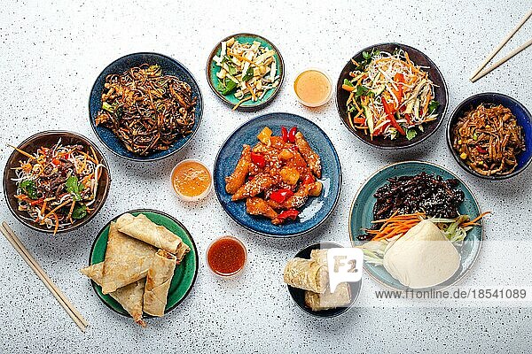 Chinesische Gerichte auf weißem Tisch: süß-saures Huhn  gebratene Frühlingsrollen  Nudeln  Reis  gedämpfte Brötchen mit glasiertem Schweinefleisch  Bankett oder Buffet im asiatischen Stil  Ansicht von oben