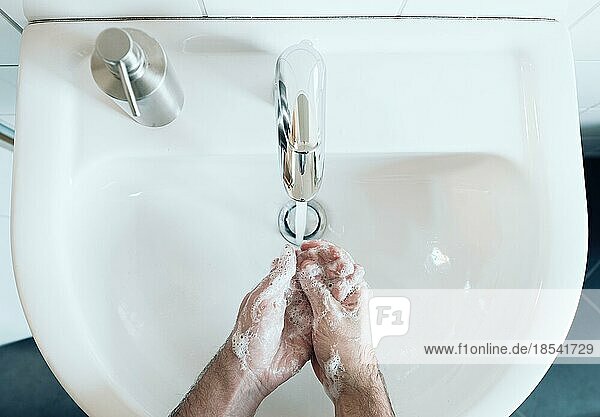 Draufsicht auf eine Person  die sich am Waschbecken im Badezimmer gründlich die Hände mit Seife und heißem Wasser wäscht  Hygienemaßnahme während der Coronavirus-Covid-19-Pandemie zur Verhinderung einer Infektion